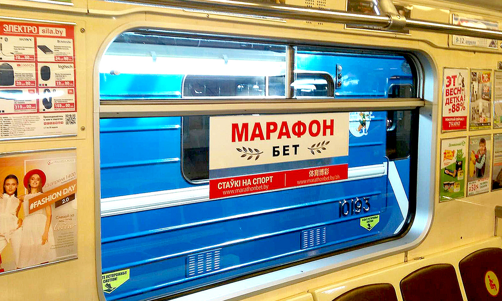 Рекламный стикер на стекле вагона минского метро с надписью «Марафон Бет», вид через окно на другой поезд